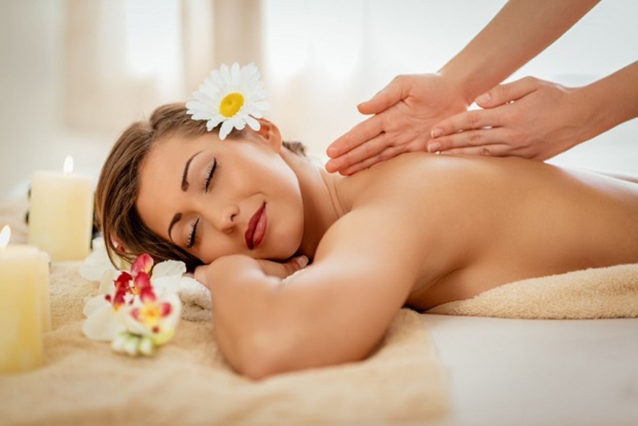 Iemand ontvangt een massage in een spa, met kaarsen en bloemen.