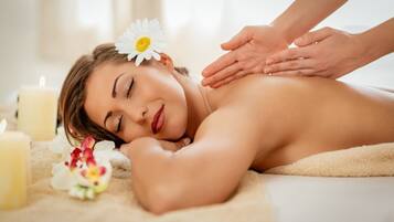 Iemand ontvangt een massage in een spa, met kaarsen en bloemen.