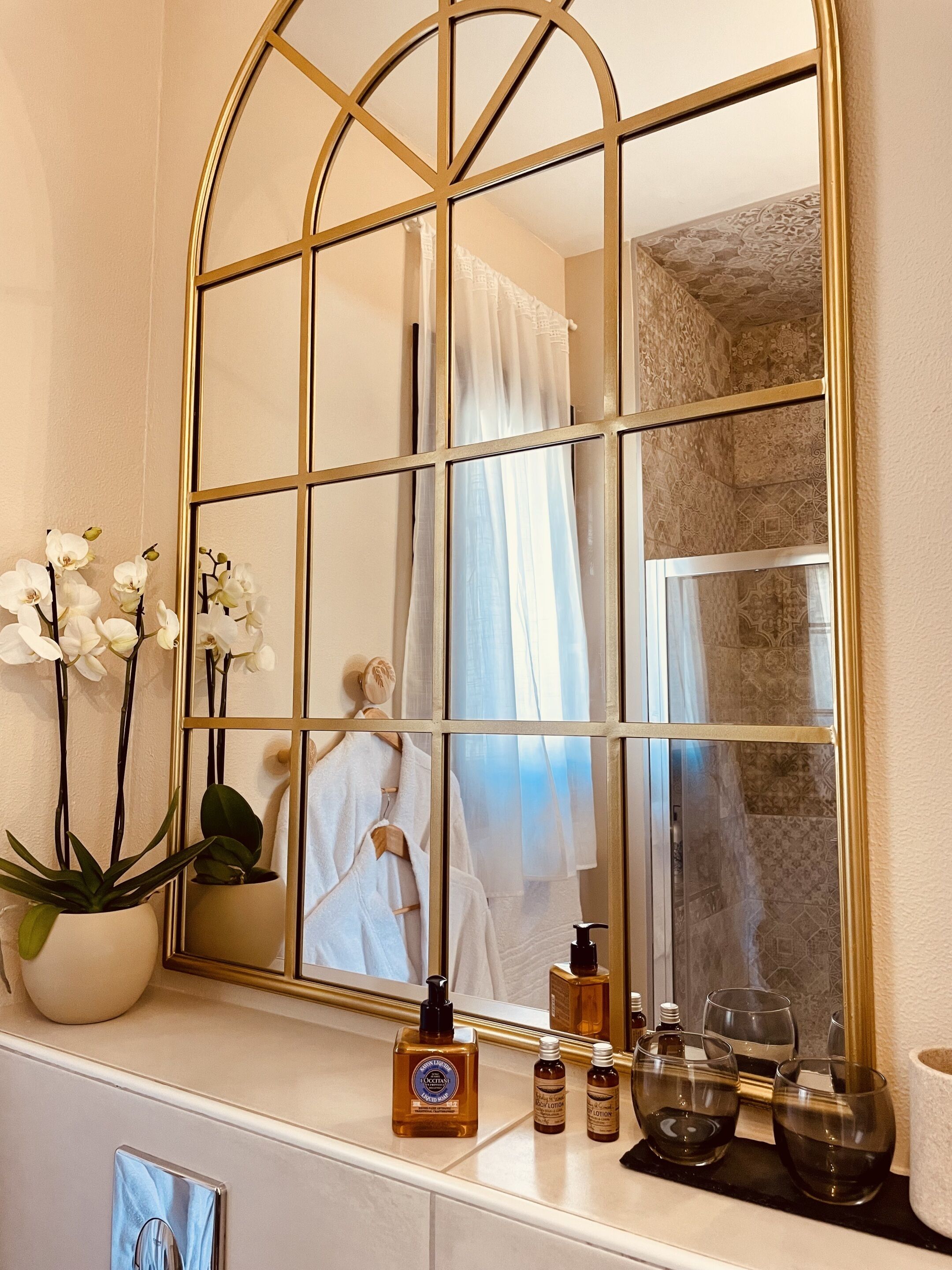 A bathroom with a large mirror, white orchids, a robe, and toiletries on the counter.