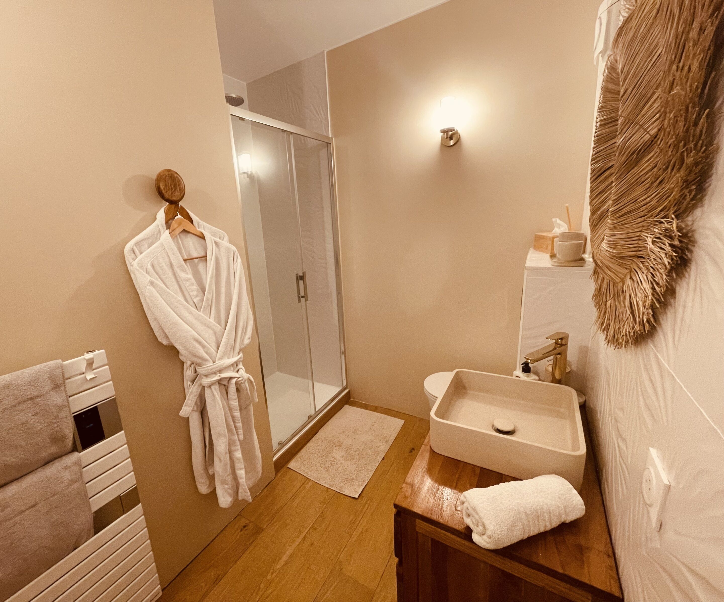 A bathroom with a glass shower door, a wooden vanity with a sink, and a towel rack with a white robe hanging.
