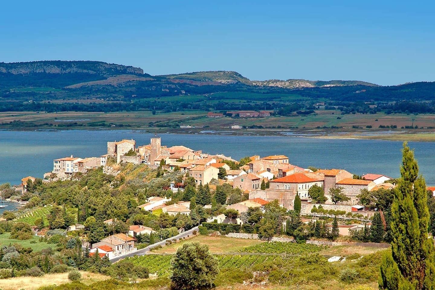 A coastal town with historic buildings, a prominent tower, and a view of the sea and hills in the background.