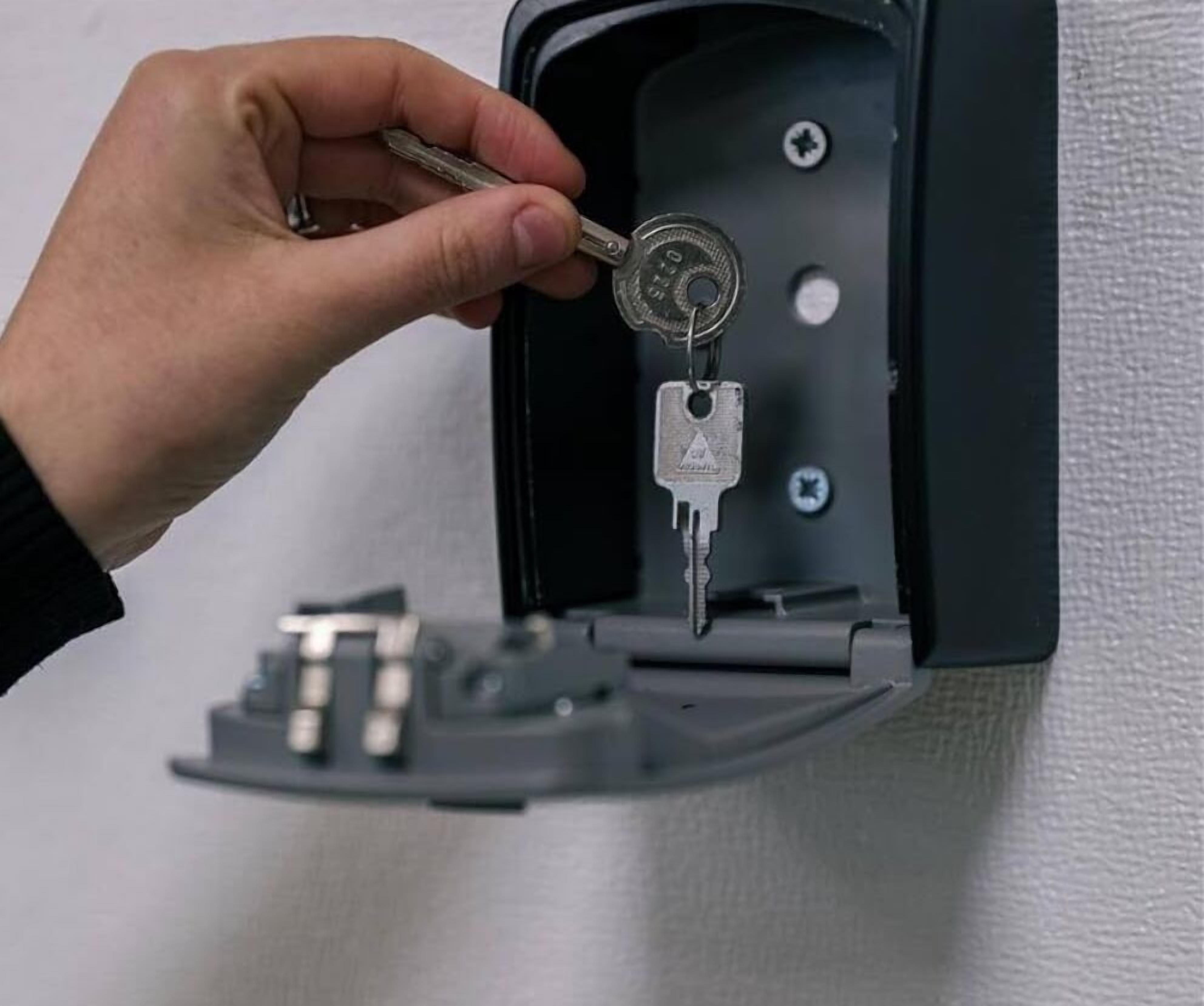A hand inserting a key into a lock on a gray outdoor electrical box.