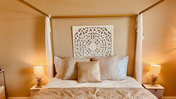 Een hemelbed met baldakijn, een decoratief wandpaneel en twee bedlampen.