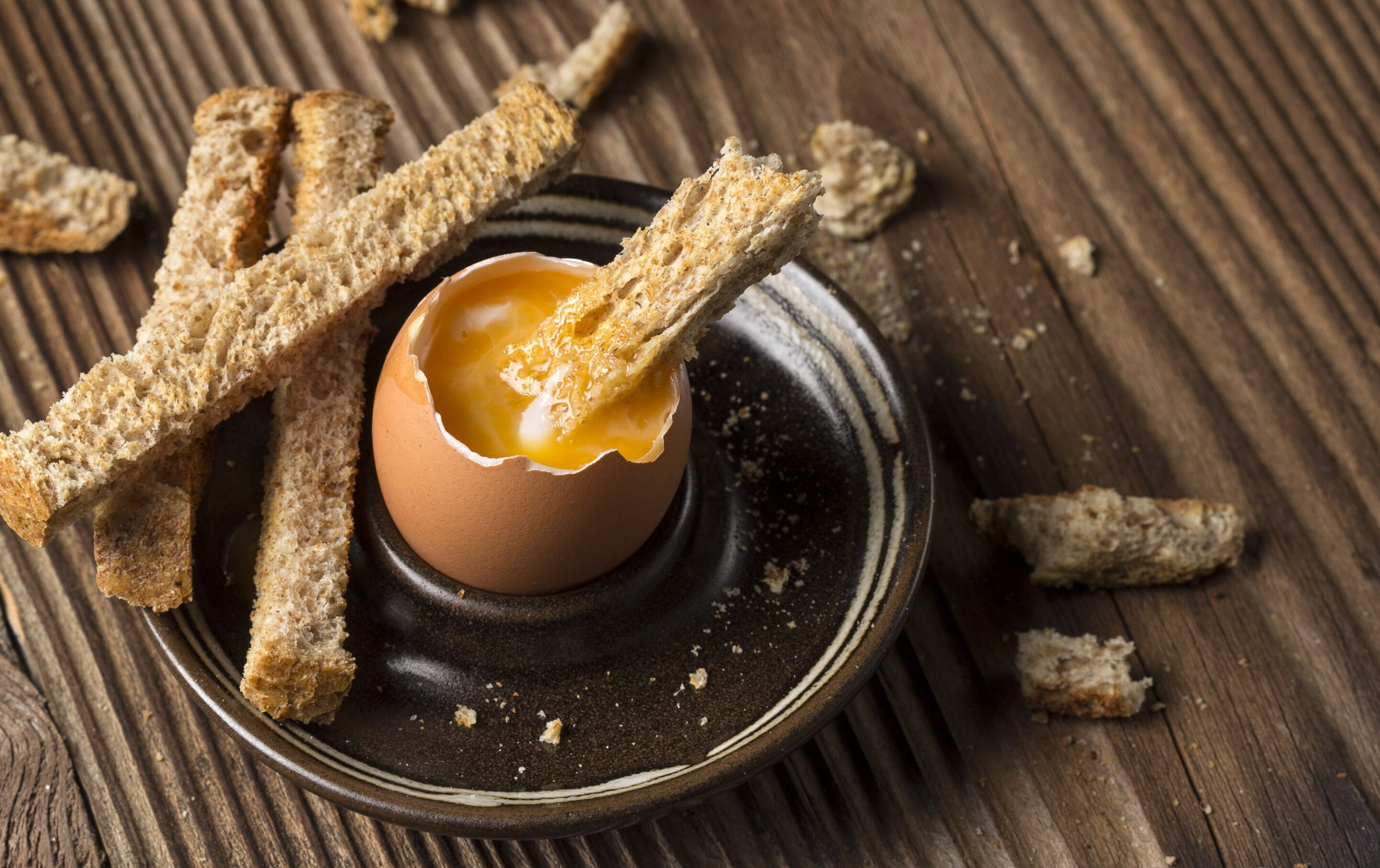 A bowl of egg yolk surrounded by breadsticks on a dark plate.