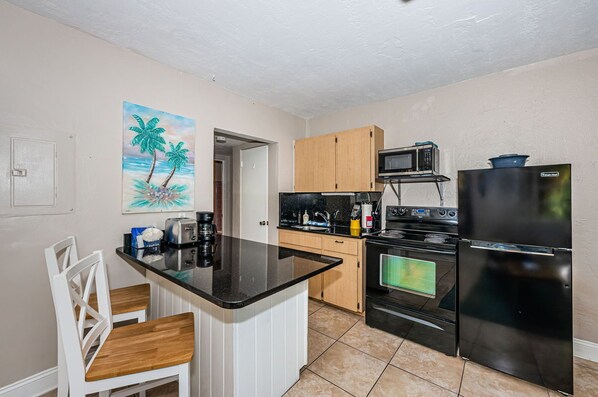 A compact kitchen with a black countertop, wooden cabinets, a microwave, a stove, and a refrigerator.