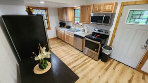 A modern kitchen with wooden cabinets, stainless steel appliances, and a black countertop. - Daisy's Riverside Log Cabin with 2 kayaks, Arcade, hot tub & recliners. (Pigeon Forge)