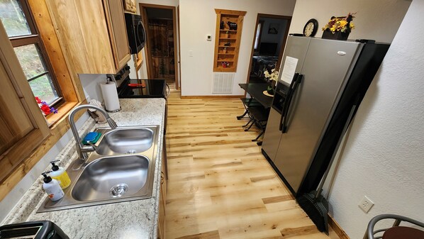 A kitchen with wooden flooring, stainless steel sinks, a refrigerator, and a microwave.