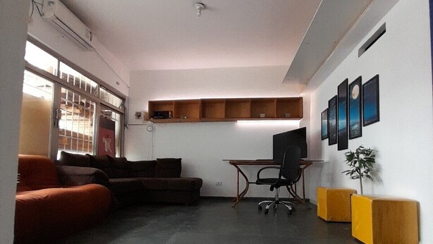 Una sala de estar moderna con piso de baldosas oscuras, un sofá, un escritorio con una silla y una planta pequeña.