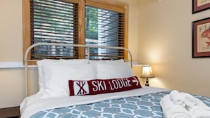 Habitación de hotel con cama, ventana con persianas, lámpara y un cuadro en la pared.