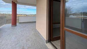 A balcony with a red pillar, a glass door, and a view of the landscape. - MiTuCasa Holiday Apartment in Rome (Vitinia)