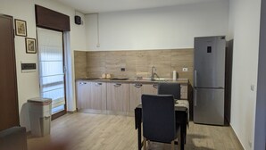 A compact kitchen with wooden cabinets, a sink, a refrigerator, and a dining area with a chair. - MiTuCasa Holiday Apartment in Rome (Vitinia)