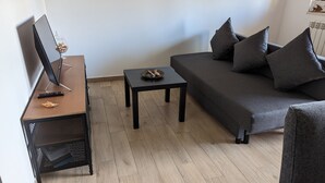 A compact living space with a sofa, a small table, a TV on a stand, and a radiator. - MiTuCasa Holiday Apartment in Rome (Vitinia)