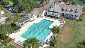 Vista aérea de una casa grande con piscina rodeada de sillones de descanso y palmeras.