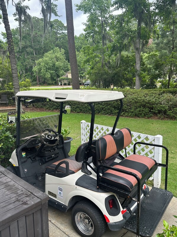 A golf cart with a white body and black and red striped seats, parked on a wooden deck.