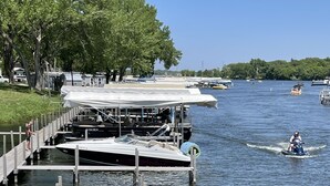 A wooden dock extending into calm water, surrounded by trees and boats.
