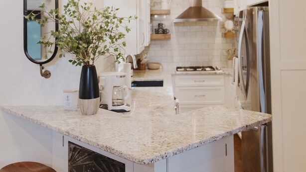 A modern kitchen with white cabinets, a granite countertop, hanging pendant lights, and a central island with stools.