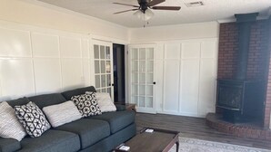A living room with a dark grey sofa, patterned pillows, a wooden coffee table, and a patterned rug. There is a fireplace and a ceiling fan visible. - Country Retreat north of Chandler (Tryon)