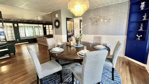 Zona pranzo con tavolo rotondo apparecchiato per sei persone, circondato da sedie a righe, un lampadario e una parete azzurra decorata con piatti ornamentali.