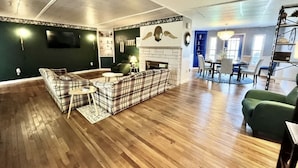 Un ampio soggiorno con pavimento in legno, divano con motivo tartan, camino e zona pranzo con sedie e tavolo.