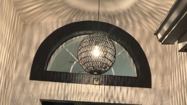 Une entrée en arc surmontée d’un plafond décoratif et d’un luminaire suspendu.