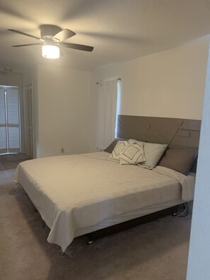 Ein Schlafzimmer mit einem Bett, einem Deckenventilator und einem Fenster mit Vorhängen.