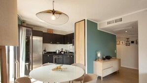 A modern kitchen with dark cabinets, a white dining table, and a pendant light. - Casa Aliméa (Calenzana)