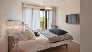 A bedroom with a bed, a TV mounted on the wall, a lamp, and a window with curtains. - Casa Aliméa (Calenzana)
