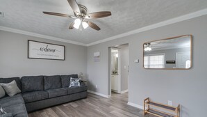 Ein Wohnzimmer mit grauem Sofa, Deckenventilator, Holzbank und großem Spiegel.