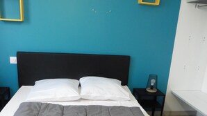 A bed with a grey quilt, a black headboard, and white pillows against a blue wall with yellow square decorations.