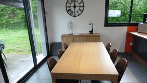 A dining area with a wooden table and chairs, a clock on the wall, and a view of the outdoors through a glass door.