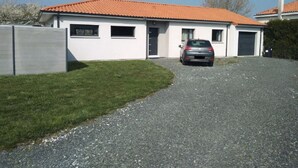 A single-story house with a red-tiled roof, a gravel driveway, and a parked car.