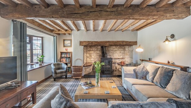 A cozy living room with exposed wooden beams, a stone fireplace, a comfortable sofa, and a television on a wooden stand. - 4 bedroom accommodation in Llysfaen, near Colwyn Bay (Llysfaen, near Colwyn Bay)