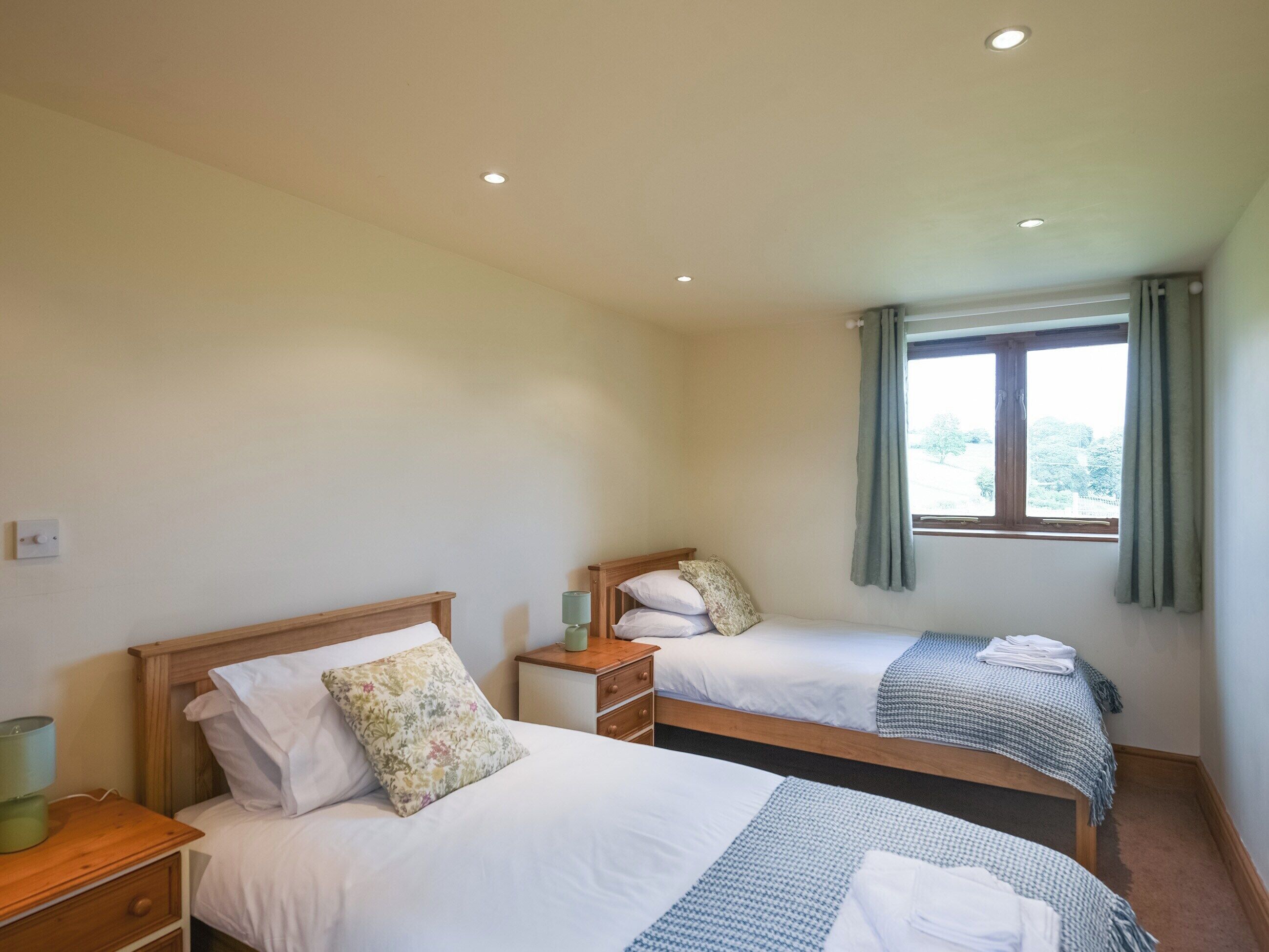 Ein Hotelzimmer mit zwei Einzelbetten, einem kleinen Nachttisch mit Lampe, einem Fenster mit Vorhängen und einer Deckenleuchte.