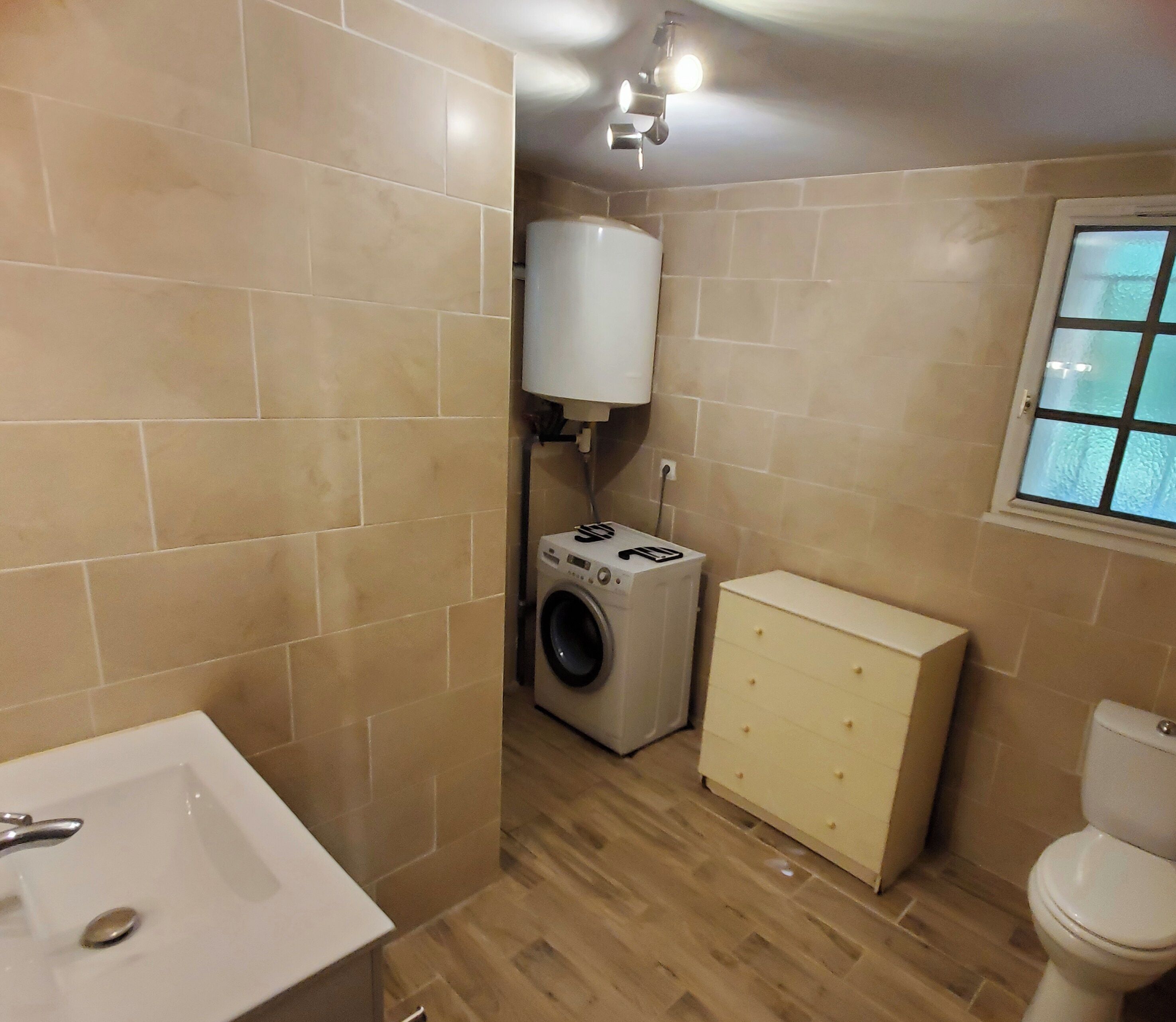 A compact bathroom with a sink, washing machine, and toilet.