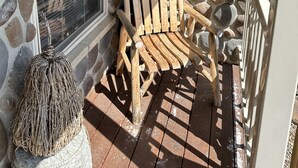 Een stoep met een stenen muur, een houten Adirondack-stoel en een raam met luiken.