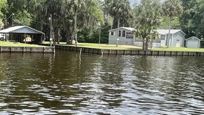 Un lago tranquilo con un muelle, rodeado de árboles y un pequeño edificio.
