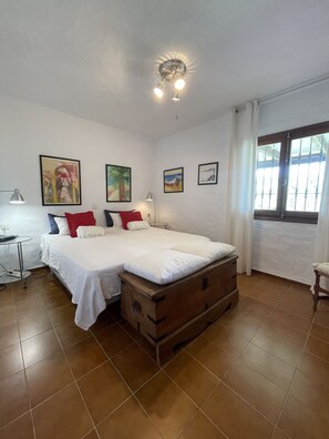 Un dormitorio con una cama doble, un cofre de madera y una ventana con cortinas.