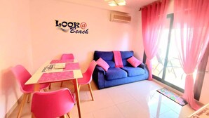A room with a dining table, chairs, a sofa, and a large window with pink curtains.