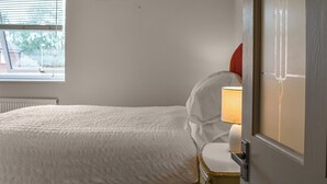 Un dormitorio con una cama, una mesita de noche con lámpara, una ventana y un radiador.