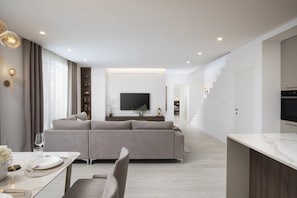 A modern living room with a grey sofa, a dining table set for two, and a TV mounted on the wall.
