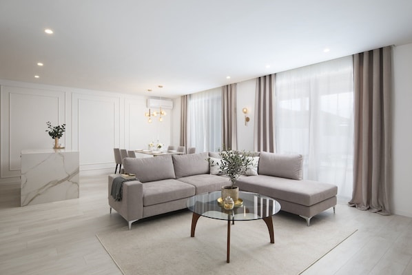 A modern living room with a sectional sofa, a glass coffee table, and a dining area with a table and chairs.