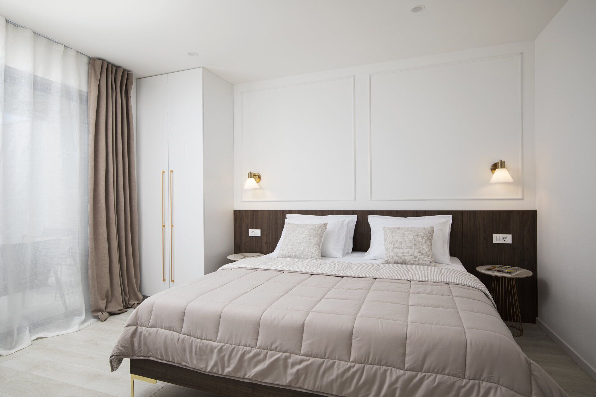 A modern bedroom with a large bed, two bedside lamps, a wardrobe, and a small side table.