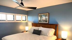 A bedroom with a bed, nightstands, a ceiling fan, and a window with blinds. - Sugar Beach Oceanfront Condo with Spectacular Views and Steps to Beach (Kihei)