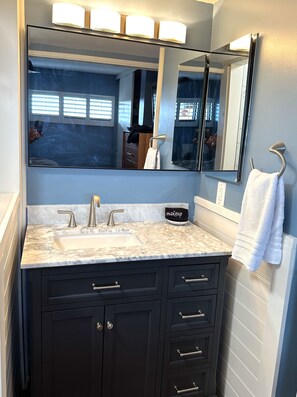 Un baño con lavamanos de mármol, armarios oscuros, un espejo grande y un perchero para toallas.