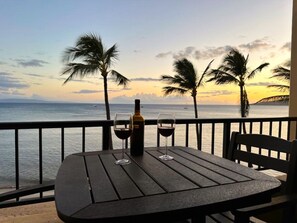 Una mesa con dos copas de vino y una botella en un balcón con vista al mar y palmeras.