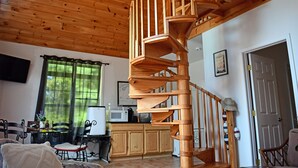 Un escalier en colimaçon en bois se trouve dans une pièce qui comprend un coin cuisine, une table à manger et des chaises.