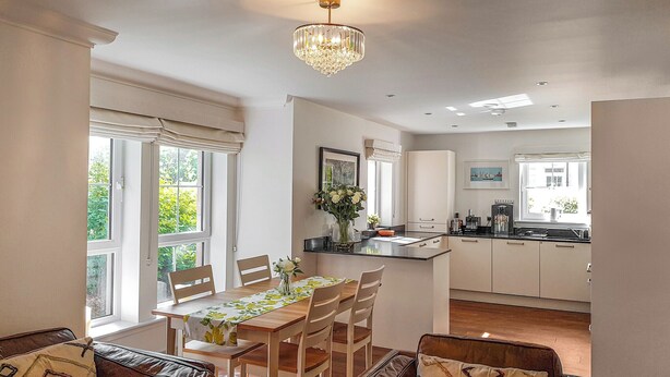 A modern kitchen with white cabinets, a dining area with a wooden table and chairs, and a chandelier. - Torrance at Abbey Park Avenue (St Andrews)