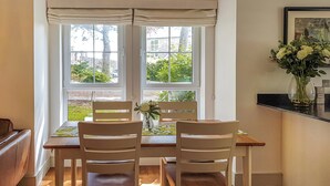 A dining area with a table and chairs, a vase with flowers, and a window with a view of greenery. - Torrance at Abbey Park Avenue (St Andrews)