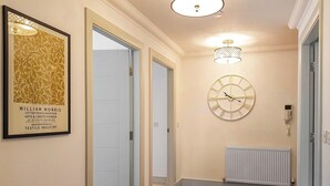 A hallway with wooden flooring, a framed poster on the wall, a wall-mounted clock, and a radiator. - Torrance at Abbey Park Avenue (St Andrews)