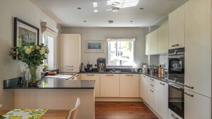 A modern kitchen with a central island, wooden flooring, and a dining area with a table and chairs. - Torrance at Abbey Park Avenue (St Andrews)